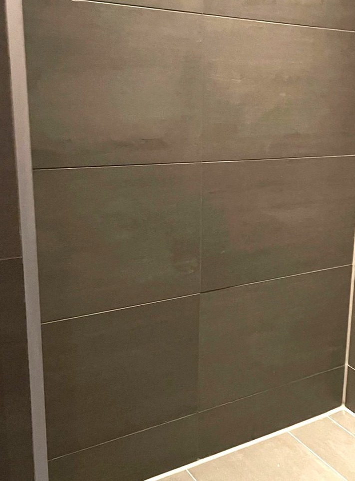 Douchewand met donkergrijze tegels en een strakke witte kitnaad langs de vloer en in de hoek