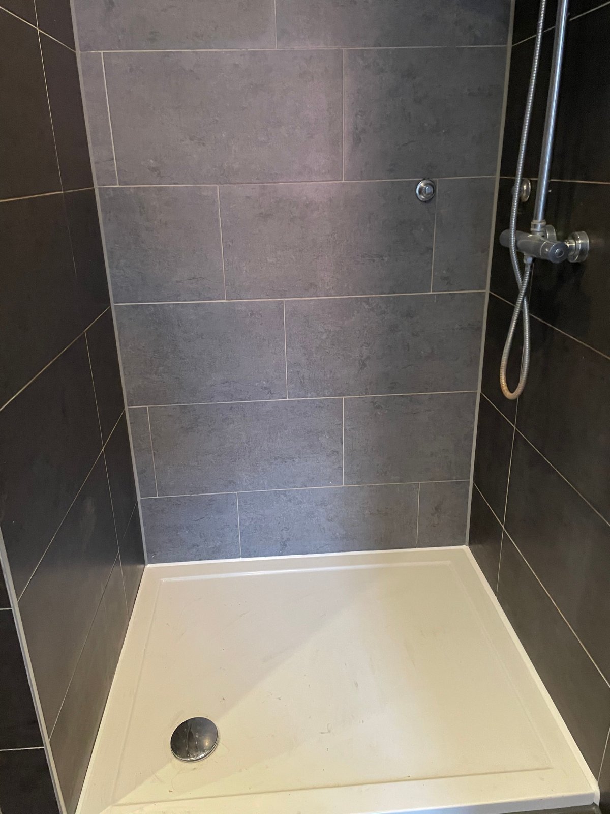 Douche met wit douchebakje, nieuwe kitnaad rondom de rand van het bakje en langs de grijze tegels