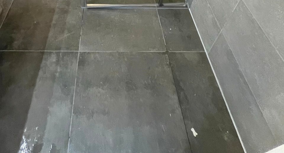 Douchevloer met donkere tegels, doucheput en de kitnaad langs de wand